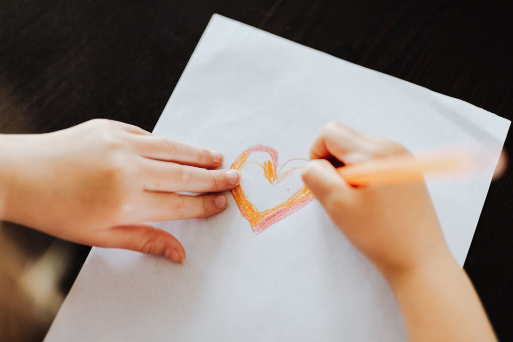 Child drawing and coloring a heart on a piece of paper.