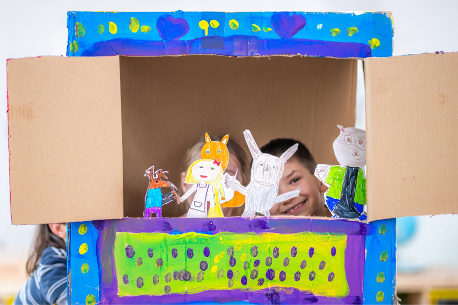 Children pretend playing with puppets in a box theater